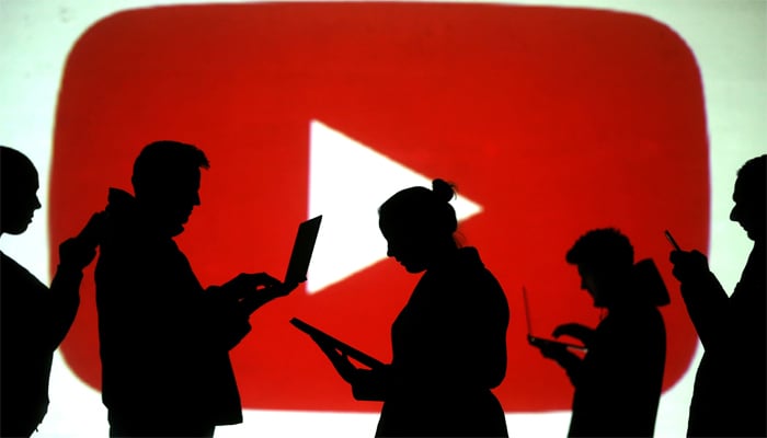 Silhouettes of laptop and mobile device users are seen next to a screen projection of YouTube logo in this picture illustration taken March 28, 2018. — Reuters