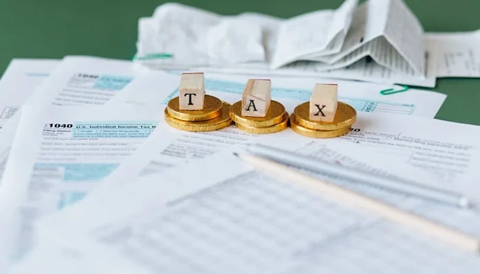 A representational image of a table where coins and cubes with tax letters written on them are placed on the papers. — Pexels