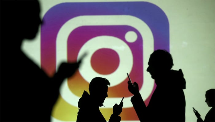 Silhouettes of mobile users are seen next to a screen projection of the Instagram logo in this picture illustration taken March 28, 2018. — Reuters